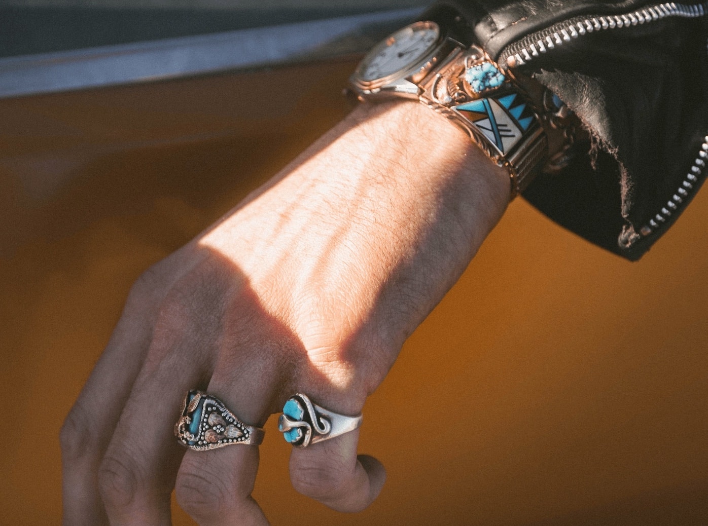 A woman hand with a watch with mosaic band ornament and two silver rings with the blue stones on orange background